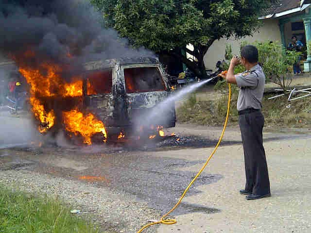 Aparat kepolisian sedang melakukan pemadaman terhadap mobil yang terbakar
